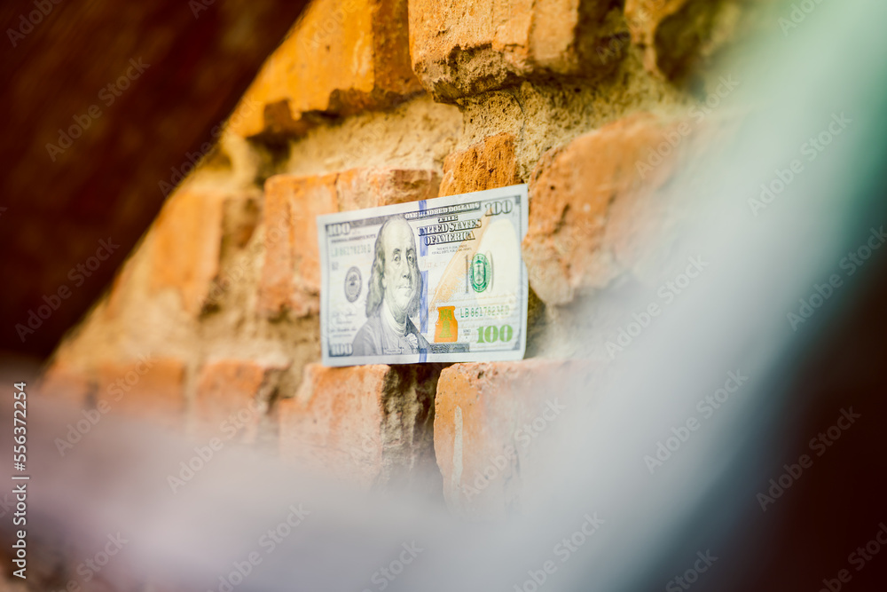A hundred dollar bill is glued to an old brick wall close-up. Old crumbling red brick wall and cash, us dollar A hundred dollar bill is glued to an old brick wall close-up. Old crumbling red brick wall and cash, us dollar