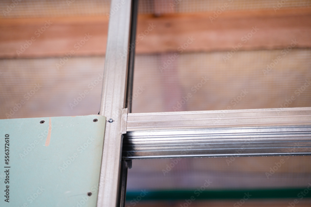 Obraz premium The beginning of the process of sheathing the frame with drywall. One sheet of moisture-resistant drywall is screwed to a metal profile in a close-up on a blurred background, bottom view