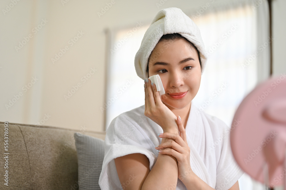Beautiful Asian woman in bathrobe cleaning her face, doing facial treatment at home. Beautiful Asian woman in bathrobe cleaning her face, doing facial treatment at home.