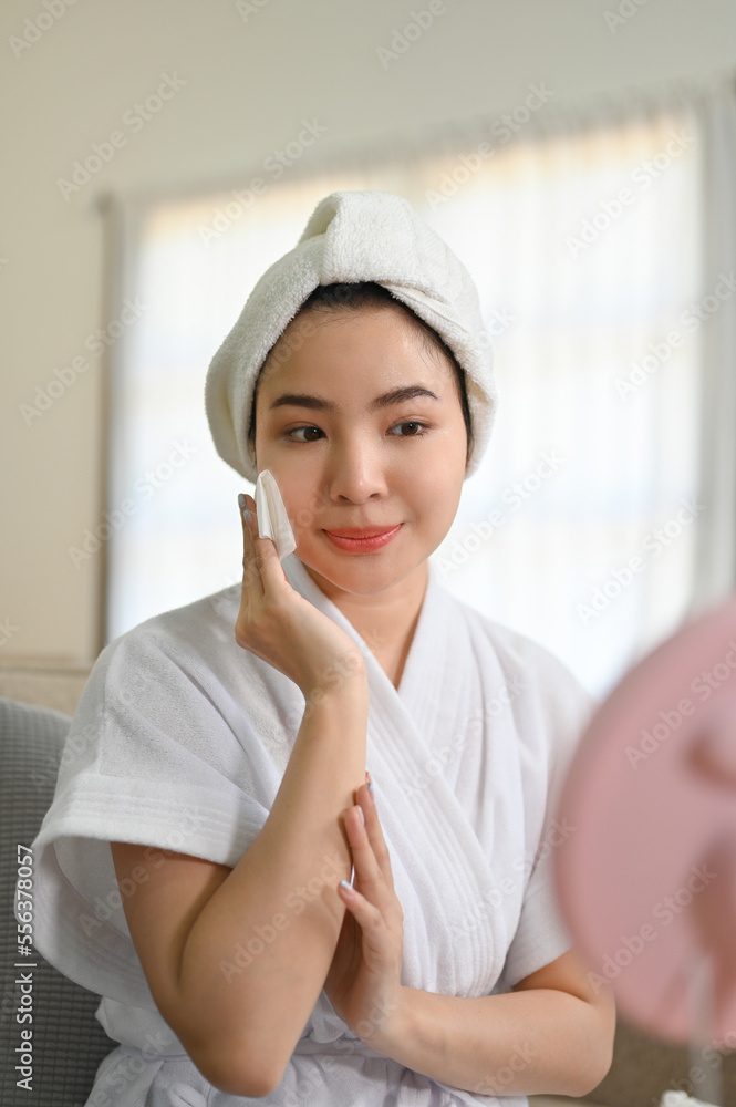 Attractive Asian woman in bathrobe cleaning her face with cleansing oil, applying moisturizer Attractive Asian woman in bathrobe cleaning her face with cleansing oil, applying moisturizer