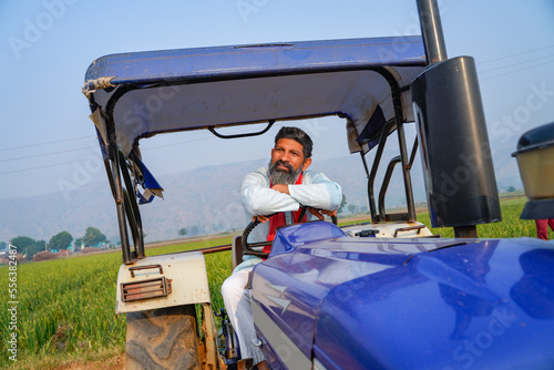 Indian farmer sitting on tractor at agriculture field.