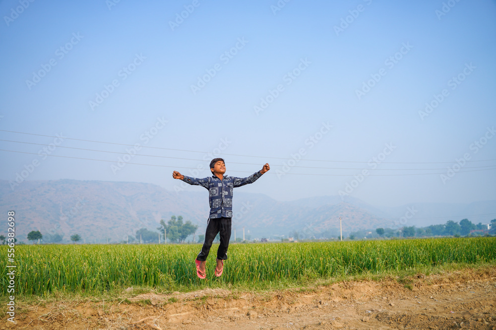 Indian little boy spreading hand and jumping at agriculture field.