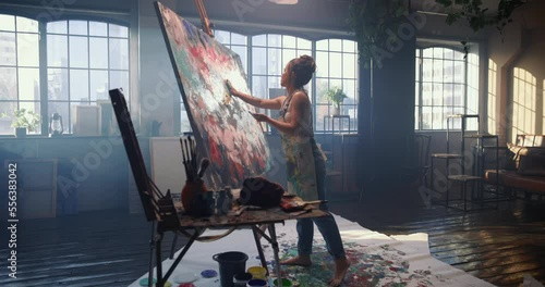 A woman in a dark workshop draws an abstract picture with her hands on a large and huge canvas. Woman artist creates art with her hands, making finishing touches, completing picture. Creation of art. photo