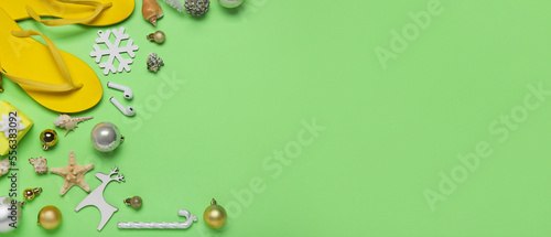 Beach flip-flops with sea shells and Christmas decor on green background with space for text