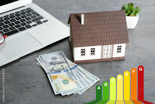 House model with dollar banknotes and laptop on grey background. Concept of energy efficiency