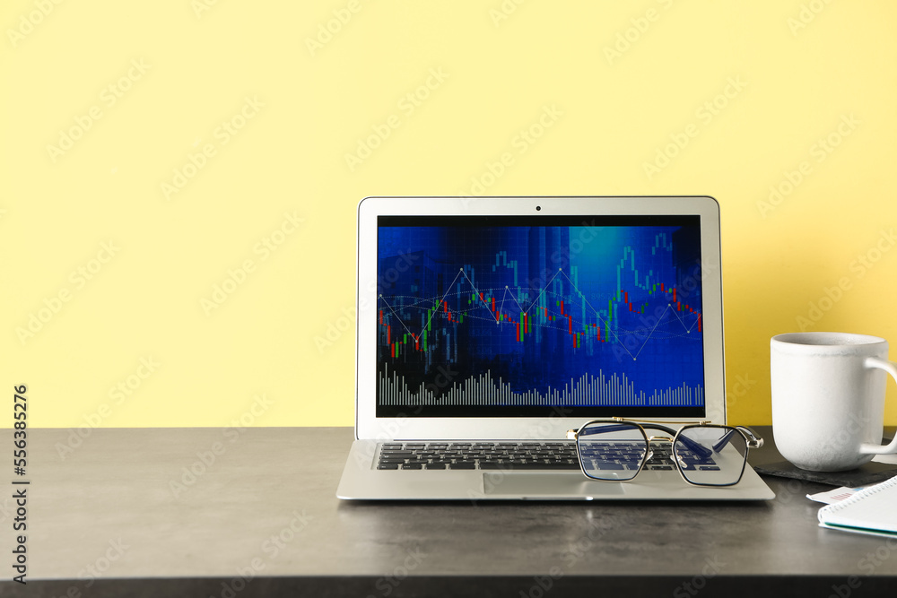 Laptop with stock data and cup of coffee on table near yellow wall. Finance trading Laptop with stock data and cup of coffee on table near yellow wall. Finance trading