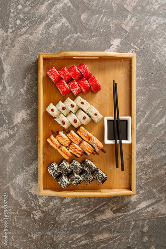 Japanese food. Set of different types of sushi served with soy sauce  wasabi  and chopsticks on wooden plate over grey background. Minimalistic style