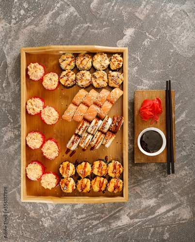 Japanese food. Set of different types of sushi served with soy sauce, wasabi and chopsticks on wooden plate over grey background. Minimalistic style