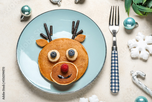 Plate with tasty reindeer pancakes and Christmas decorations on light background