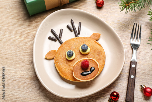 Plate with tasty reindeer pancakes and Christmas decorations on wooden background