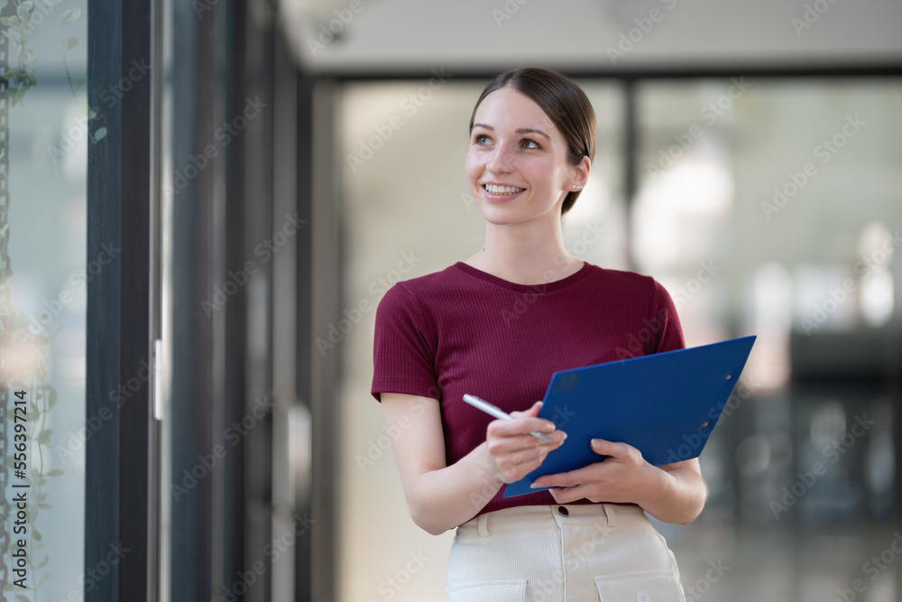 Attractive businesswoman standing and thinking while holding a pen and a folder of documents. Attractive businesswoman standing and thinking while holding a pen and a folder of documents.