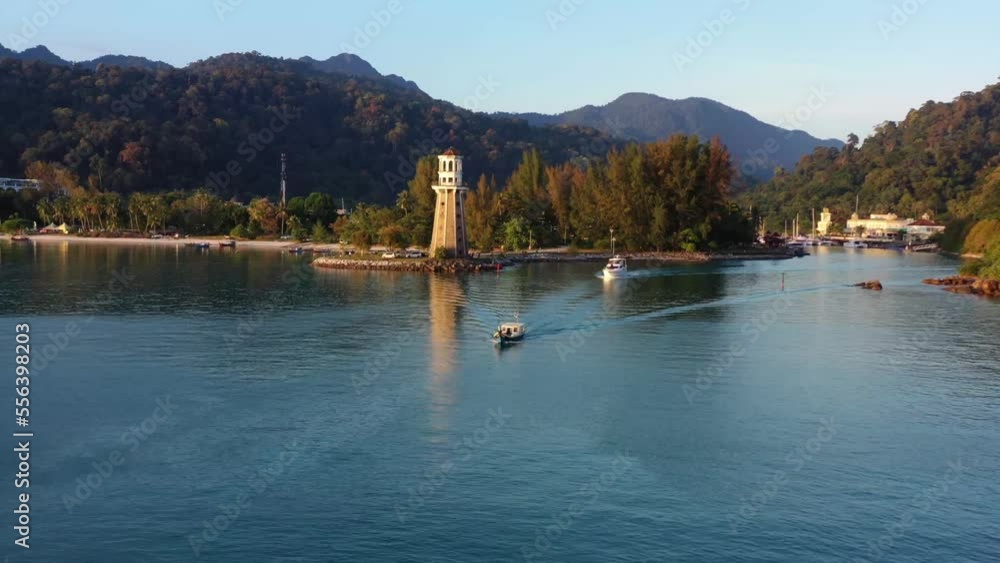 Aerial flyover capturing fishing boat and yacht sailing out from telaga harbour marine with perdana quay light house on the promontory and mountain landscape in the background at Langkawi island Aerial flyover capturing fishing boat and yacht sailing out from telaga harbour marine with perdana quay light house on the promontory and mountain landscape in the background at Langkawi island