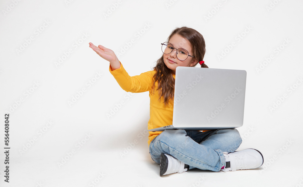 Smiling little caucasian girl having fun or playing games with virtual friends using laptop sitting cross-legged on the floor, happy little kid pointing to free space. generation z kids Smiling little caucasian girl having fun or playing games with virtual friends using laptop sitting cross-legged on the floor, happy little kid pointing to free space. generation z kids