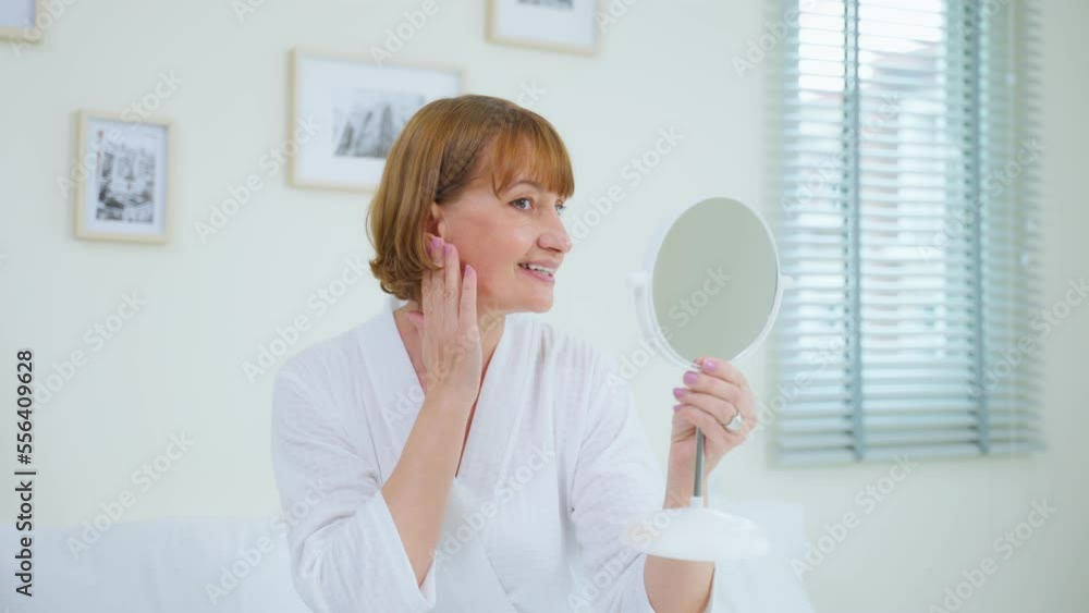 Caucasian senior woman looking at mirror after apply lotion on face. Caucasian senior woman looking at mirror after apply lotion on face.
