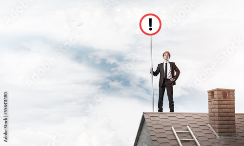 Businessman on house top showing sign with exclamation mark. Mix