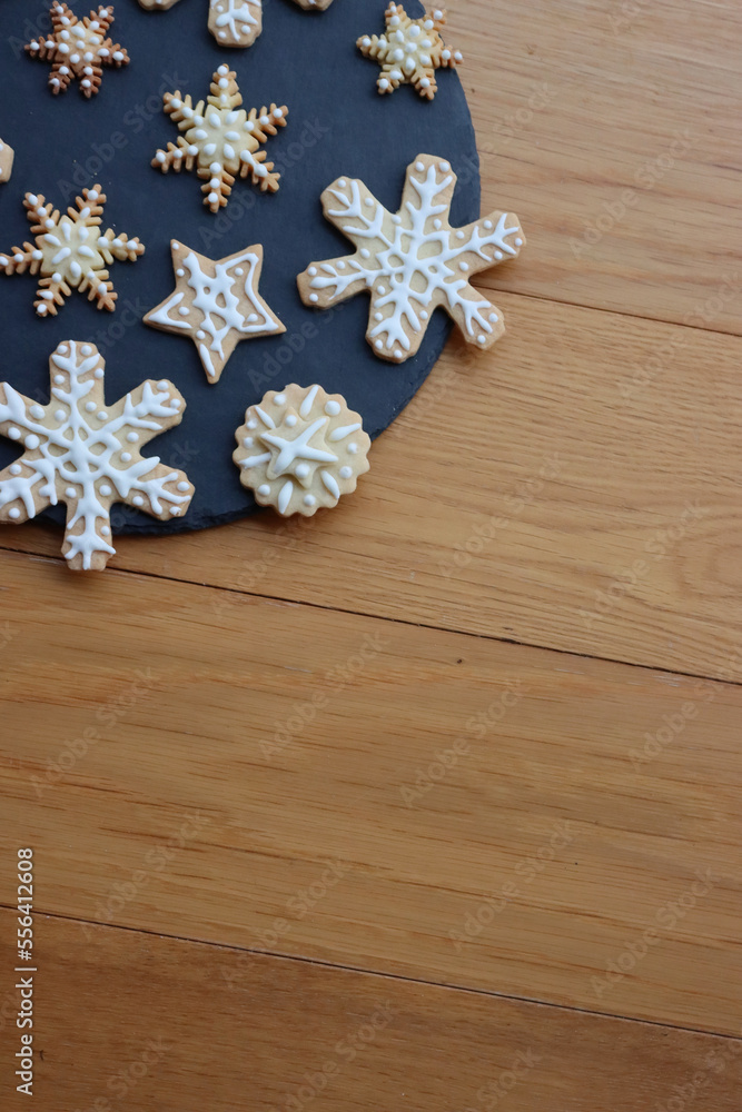 Festive gingerbread cookies in shape of Stars and Snowflakes on a black slate stone plate on wooden table Festive gingerbread cookies in shape of Stars and Snowflakes on a black slate stone plate on wooden table