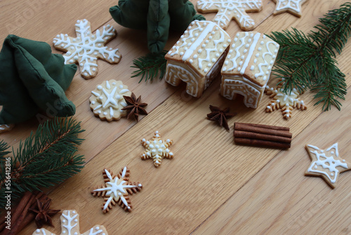 Small Gingerbread houses with many gingerbread cookies in shape of stars and snowflake  on wooden table with pine branches, cinnamon and star anise spices on selective fcous photo