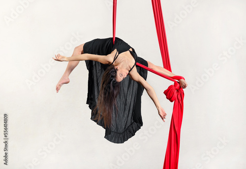 Young flexible woman hanging on aerial silks against white background