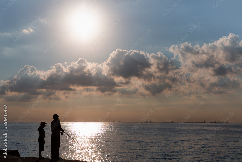 Silhouette of girl with her father fishing at the seaside