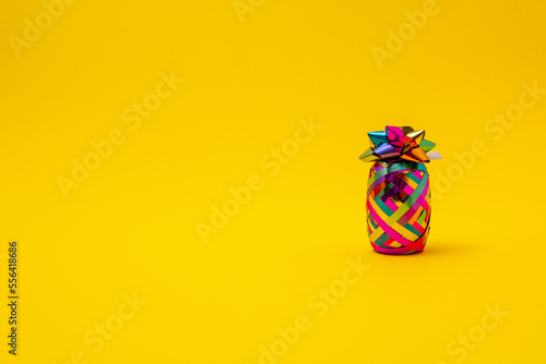 Pineapple made of colorful ribbon for gift wrapping and bow for Christmas, New year, birthday or anniversary on a yellow background. Minimal creative concept for a trendy party.