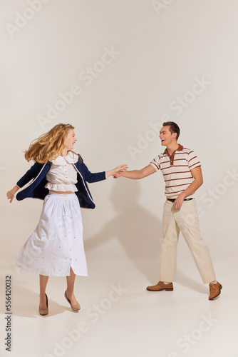 Excited young, beautiful, stylish couple in vintage style fashion clothes dancing isolated over light background. 60s, 70s american culture concept