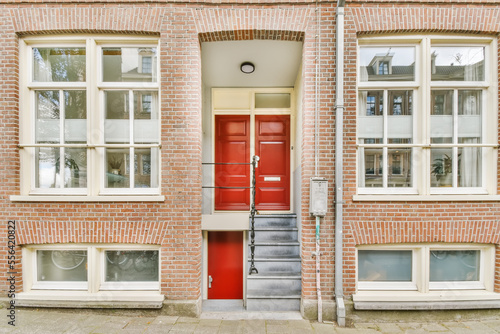 a red door in front of a brick building with two windows and an open fire hydrae on the side