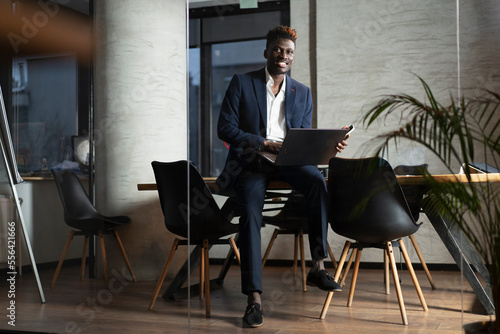 Portrait of successful businessman in office. Young smiling man using the laptop.