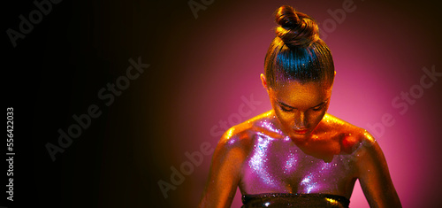 Fashion art portrait. Model girl in colorful bright sparkles, gold and pink skin, neon lights posing in studio, beautiful woman, trendy glowing sequins make-up. Design. Make up. Glitter Vivid makeup
