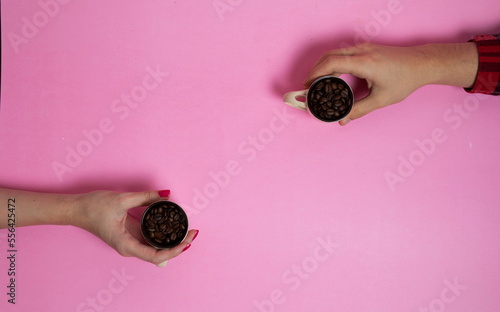 two cups of coffee full of coffee beans in hands, on a pink background. photo