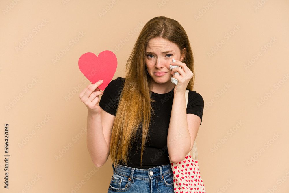 Young redhead woman holding a valentines day gift, love concept, isolated on beige background Young redhead woman holding a valentines day gift, love concept, isolated on beige background