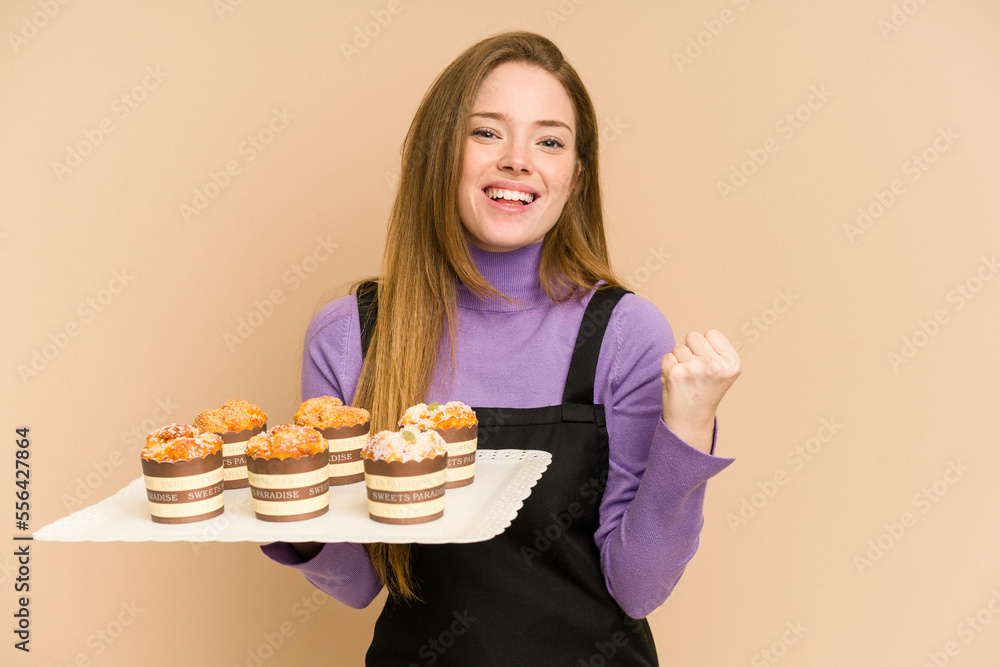 Young redhead woman holding a muffins tray cut out isolated Young redhead woman holding a muffins tray cut out isolated