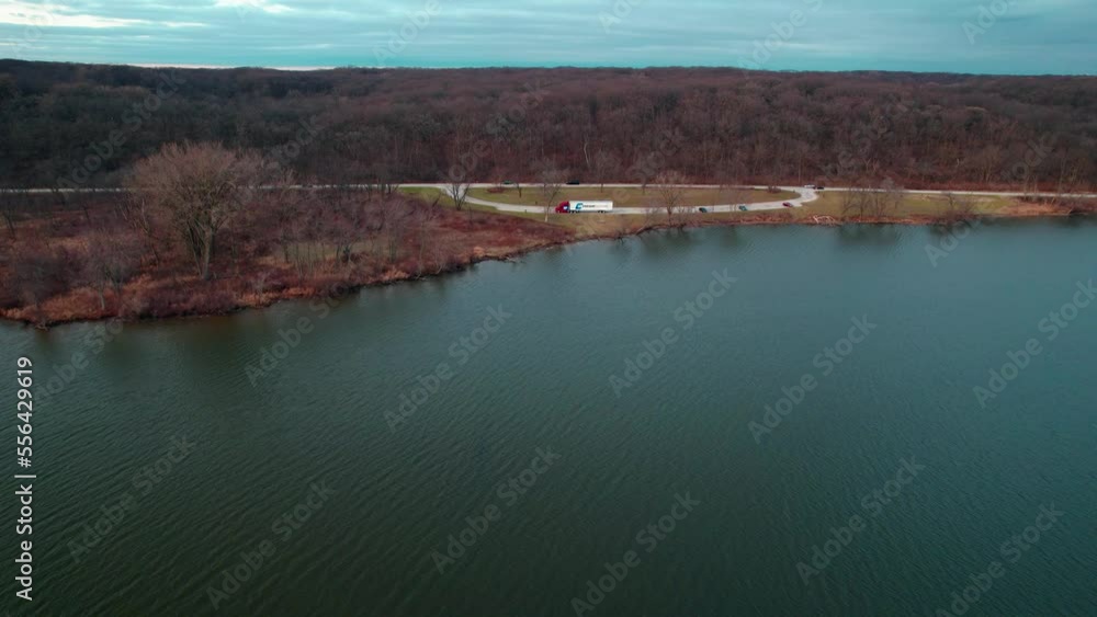 cinematic aerial of a red semi truck and white trailer parked on side of a lake. Autumn 2022. Location: saganashkee slough woods, willow springs Illinois, usa. cinematic aerial of a red semi truck and white trailer parked on side of a lake. Autumn 2022. Location: saganashkee slough woods, willow springs Illinois, usa.