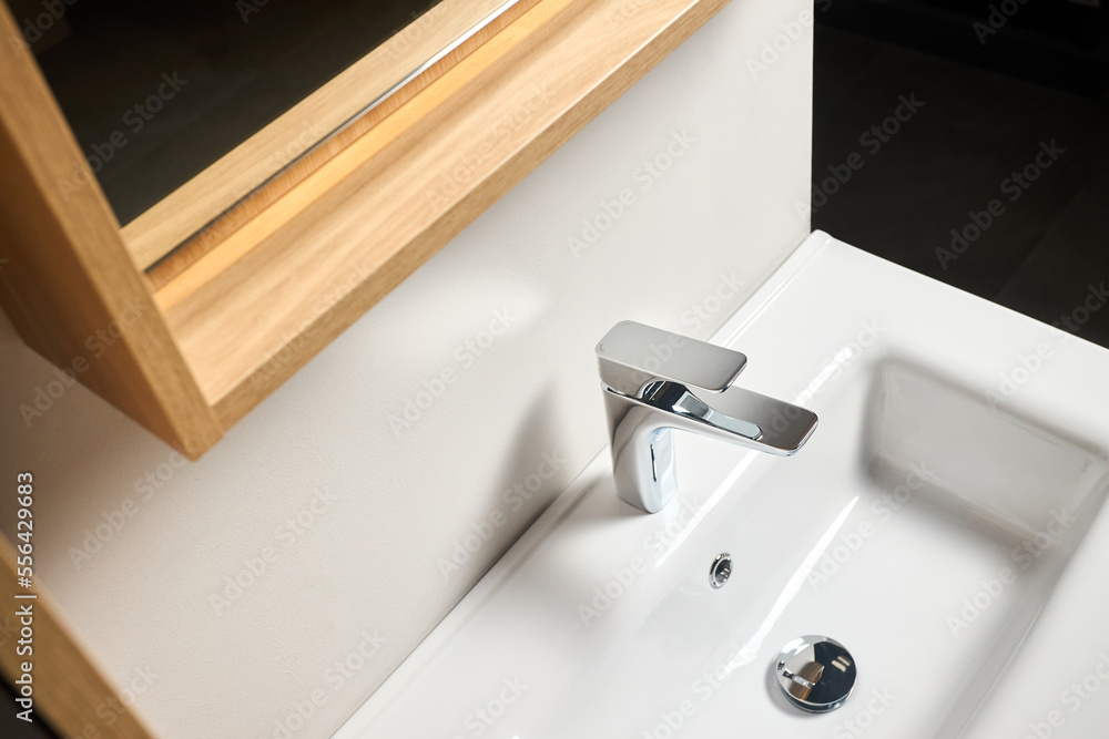 Fototapeta premium Interior of bathroom with washbasin mirror cabinet over the sink and faucet modern loft flat minimalistic design with modern countertop basin, illuminated mirror and wooden PVC cupboard.