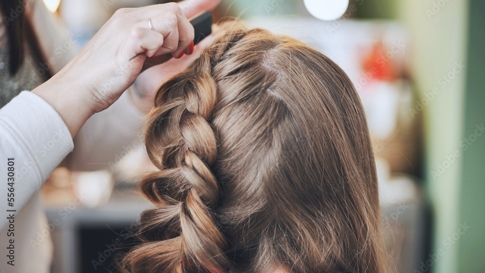 The girl makeup artist makes a braid for the model.