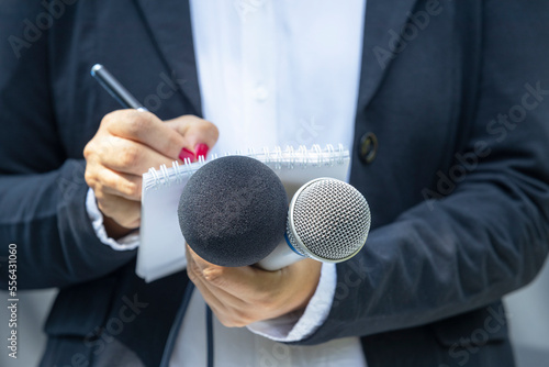 Female journalist at press conference or media event, holding microphone and writing news photo