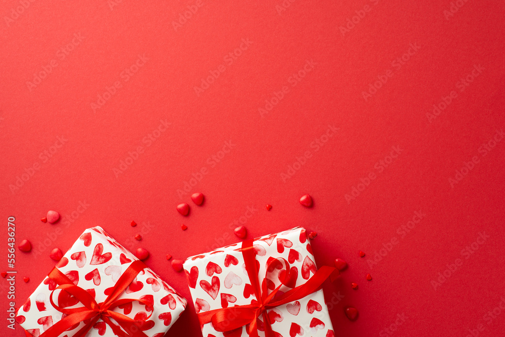 Valentine's Day concept. Top view photo of present boxes and heart shaped sprinkles on isolated red background with empty space Valentine's Day concept. Top view photo of present boxes and heart shaped sprinkles on isolated red background with empty space