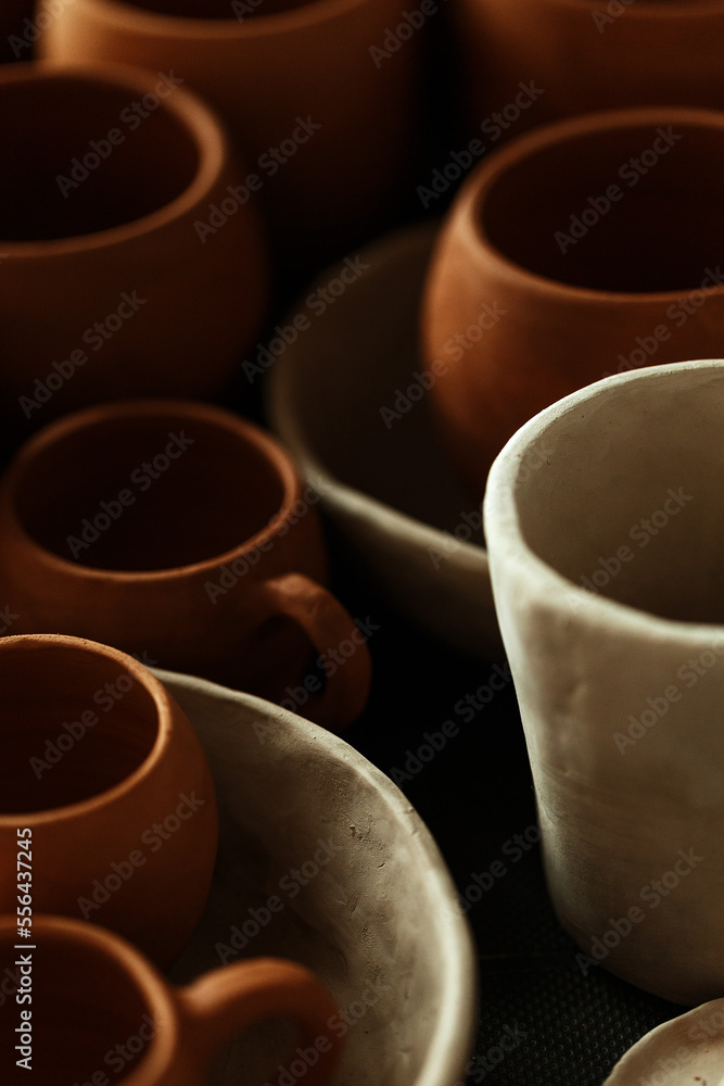 A close-up of various drying clay tableware on a shelf. A pottery studio concept. Craftmade dishes, bowls, pots, mugs of different colors. Cozy view. workshop with ceramic dishware A close-up of various drying clay tableware on a shelf. A pottery studio concept. Craftmade dishes, bowls, pots, mugs of different colors. Cozy view. workshop with ceramic dishware