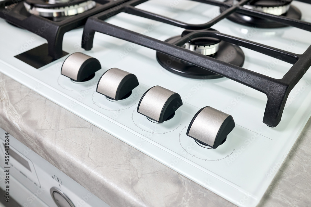 Hob cooker stove oven made of white glass grill stainless steel control knobs selective focus over out of focus oven with burner on countertop made of ceramic stoneware background. Hob cooker stove oven made of white glass grill stainless steel control knobs selective focus over out of focus oven with burner on countertop made of ceramic stoneware background.