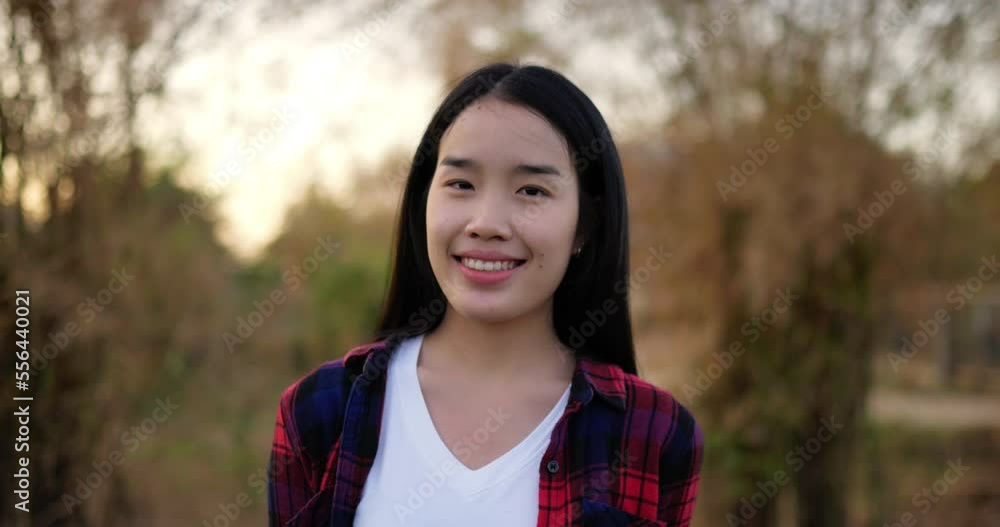 Portrait of an Asian young happy farmer woman looking at camera and smiling with a farmland background. Agriculture farming concept. Slow motion. Portrait of an Asian young happy farmer woman looking at camera and smiling with a farmland background. Agriculture farming concept. Slow motion.