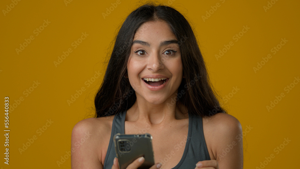 Close up Indian girl woman female lady with mobile phone win victory winning showing thumb up achieve success recommend smartphone app online web application super gesture in studio yellow background Close up Indian girl woman female lady with mobile phone win victory winning showing thumb up achieve success recommend smartphone app online web application super gesture in studio yellow background