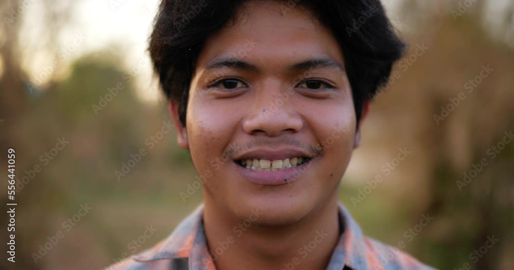 Portrait Close up of an Asian young happy farmer man looking at camera and smiling with a farmland background. Agriculture farming concept. Slow motion. Portrait Close up of an Asian young happy farmer man looking at camera and smiling with a farmland background. Agriculture farming concept. Slow motion.