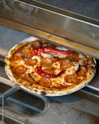 Baking pizza in pizzeria. Pizza with pepperoni, cheese and hot peppers on roasting pan. Pizza in oven. Hot freshly baked pizza. Italian food. Soft focus.