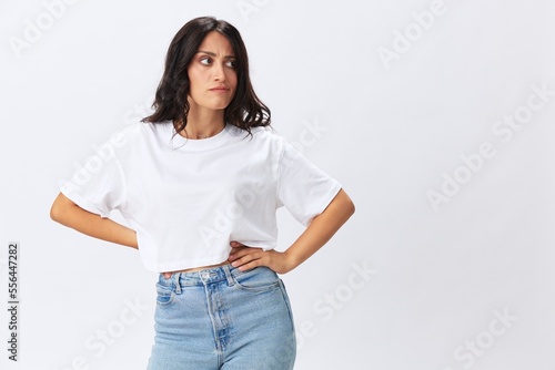 Woman in white t-shirt on white background brunette hands up gestures and signals poses in jeans emotion, lifestyle smiles, copy space