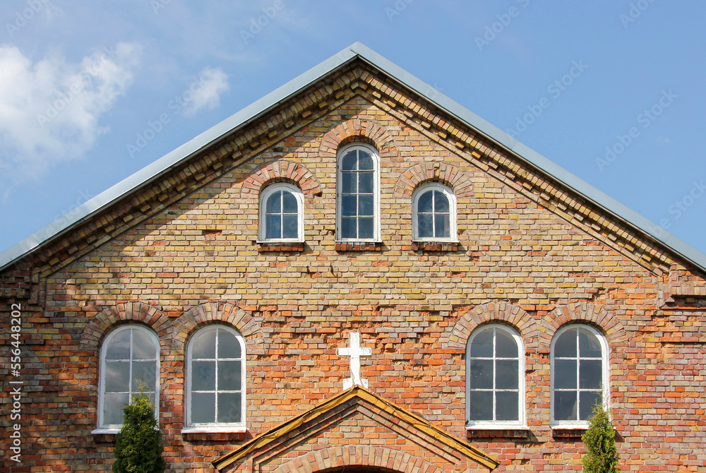 A red brick church exterior with arc windows and a cross in the center of the facade. A red brick church exterior with arc windows and a cross in the center of the facade.