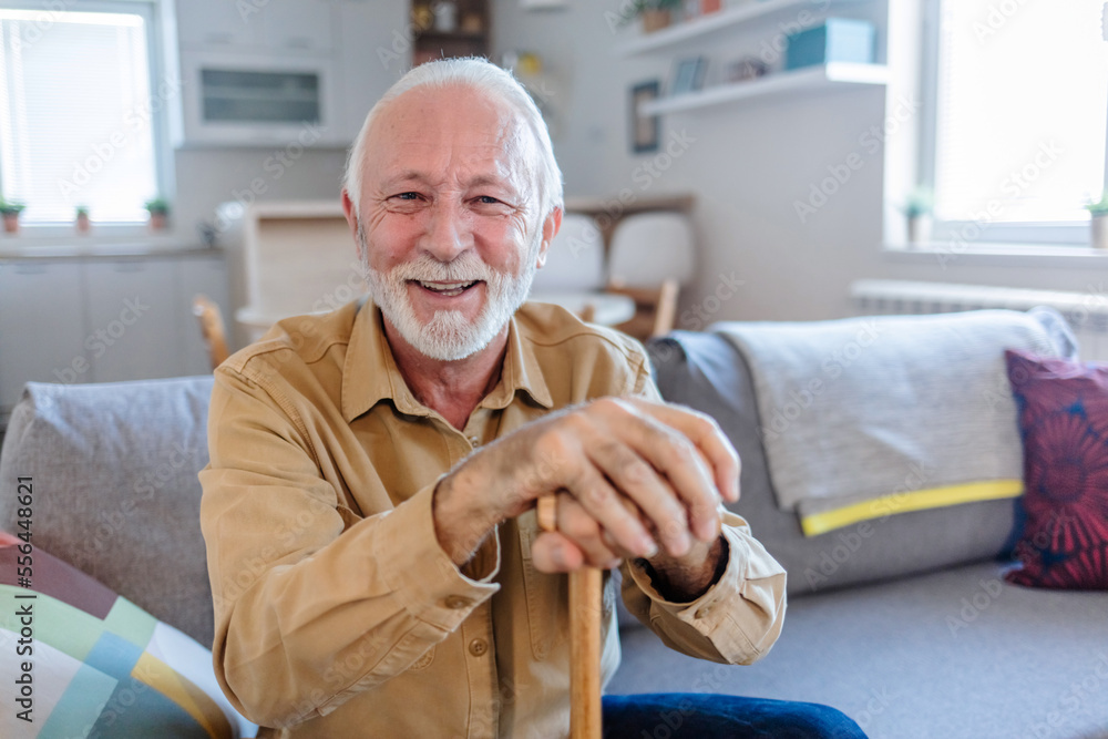 Shot of an elderly man sitting on the couch with a walking stick at home. Senior man leaning in his walking stick at home.