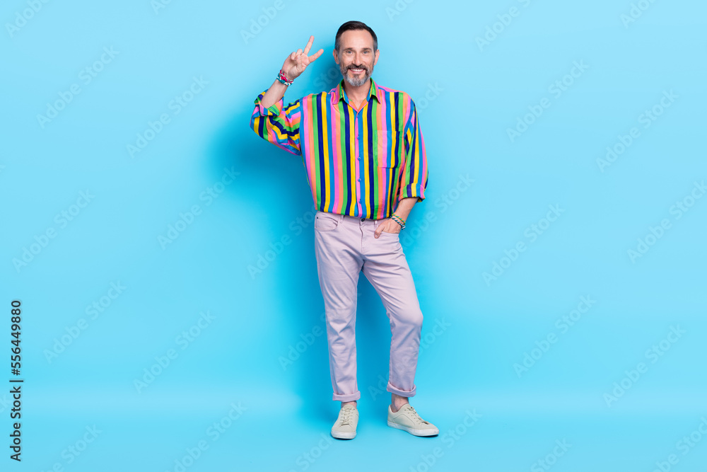 Full length photo of attractive groomed cheerful man raise hand demonstrate v-sign good mood isolated on blue color background Full length photo of attractive groomed cheerful man raise hand demonstrate v-sign good mood isolated on blue color background