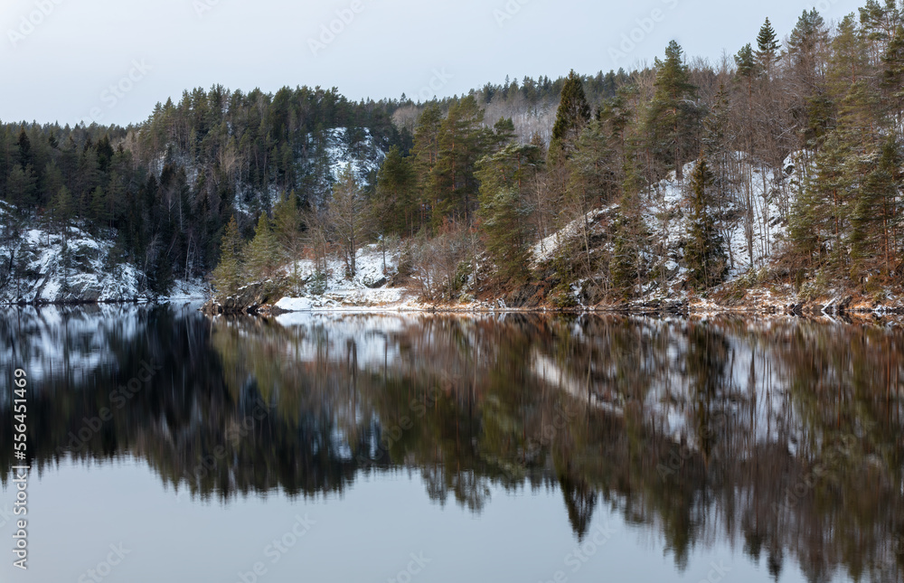 Winter landscape with forest and snow covered rocks, Beauiful reflection in the lake waters.