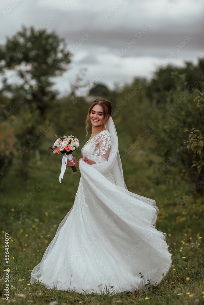 a young beautiful bride poses with a wedding bouquet against the background of nature; the girl is dressed in a white wedding dress; a moment on the wedding day; happy girl expresses her emotions a young beautiful bride poses with a wedding bouquet against the background of nature; the girl is dressed in a white wedding dress; a moment on the wedding day; happy girl expresses her emotions