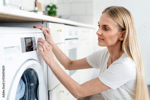 young woman turn on washing machine at home