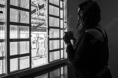 Uma mulher, solitária, segurando uma caneca de chá e olhando na janela. Imagem em preto e branco. photo
